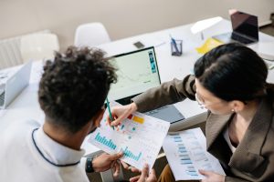 This imagine shows two professionals working at a desk and holding papers with multiple graphs. One of them is explaining a graph to the other.